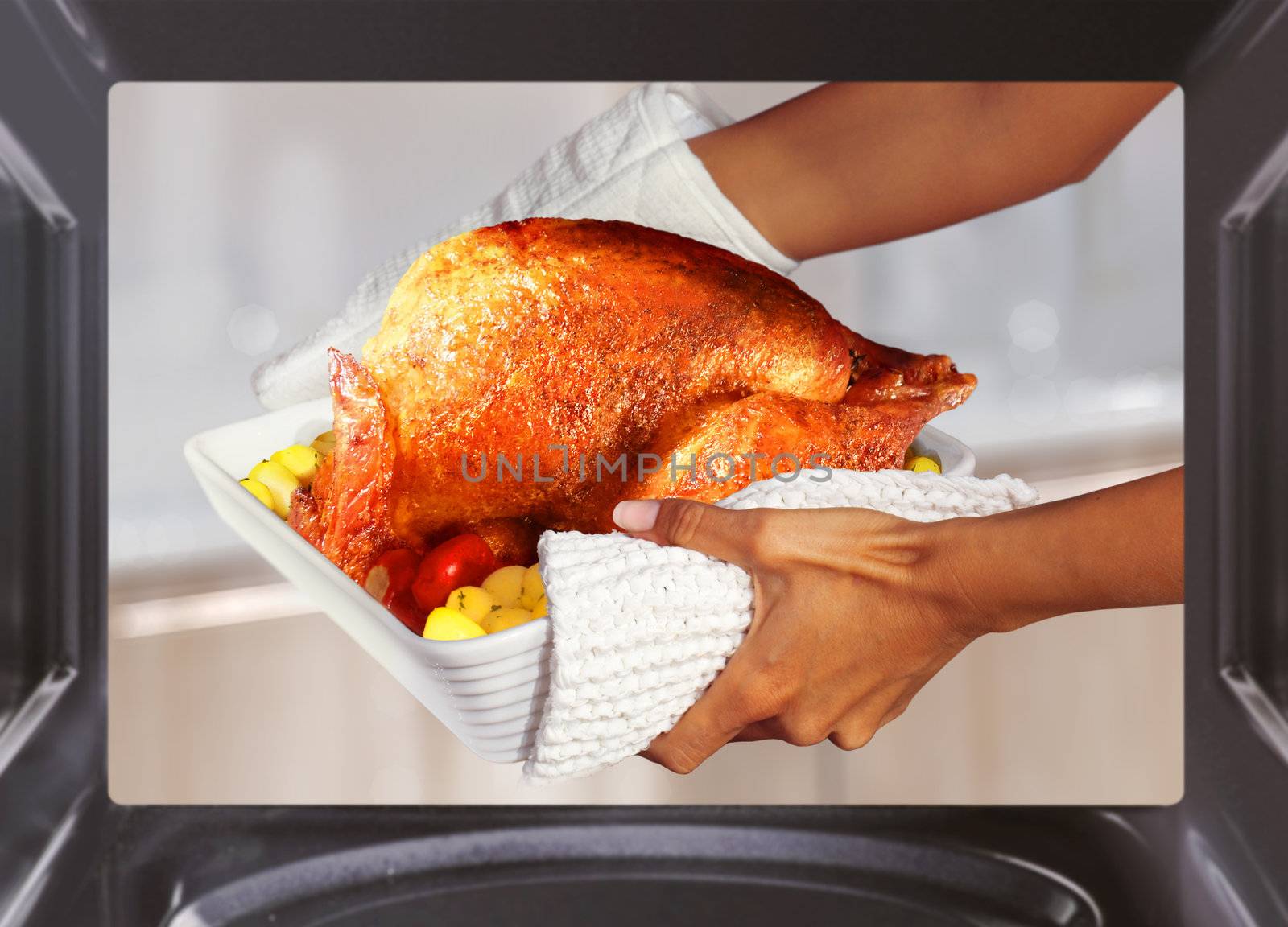 hands of woman is taking out turkey with potato from oven