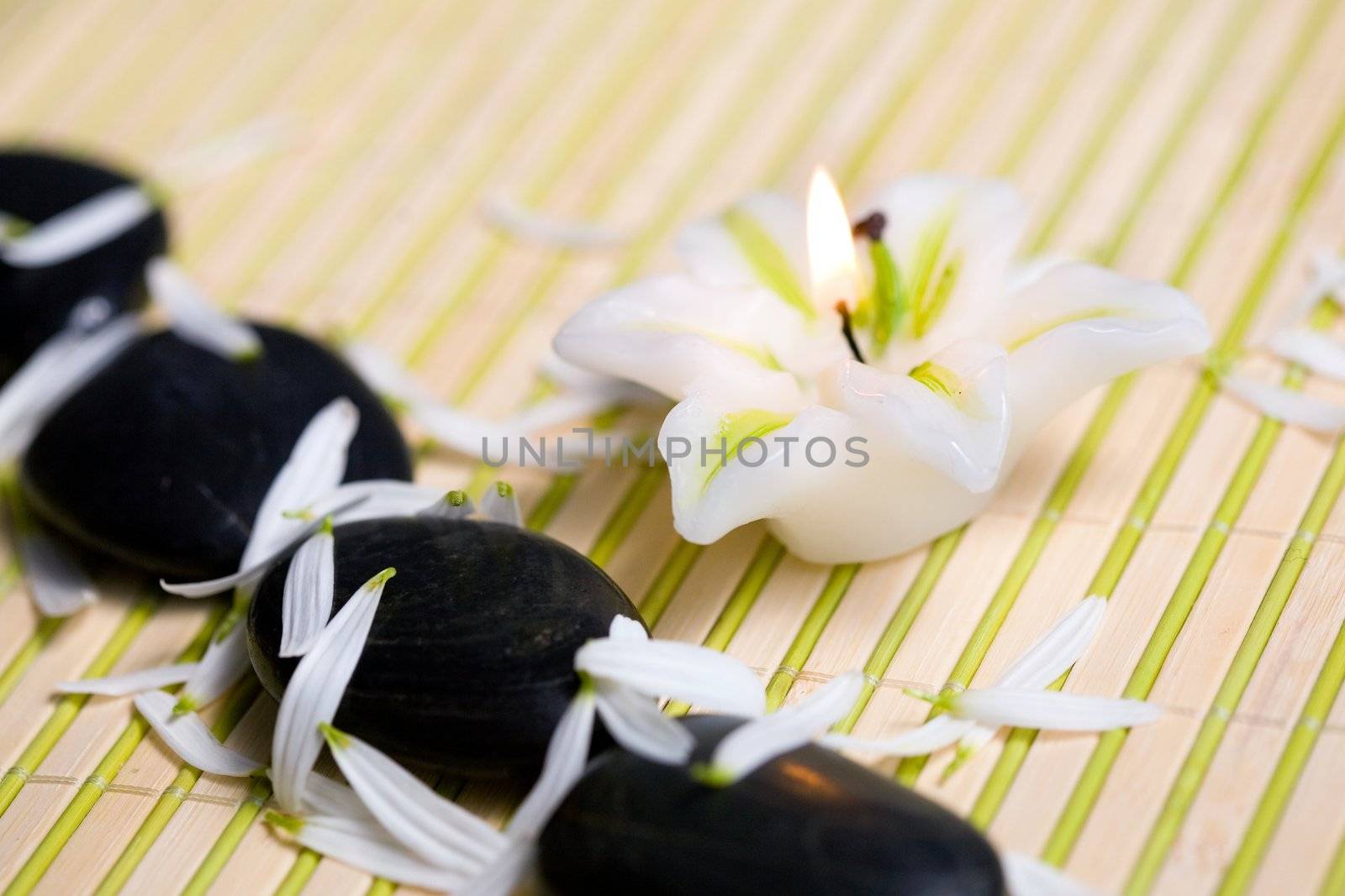A burning candle and black stones with petals
