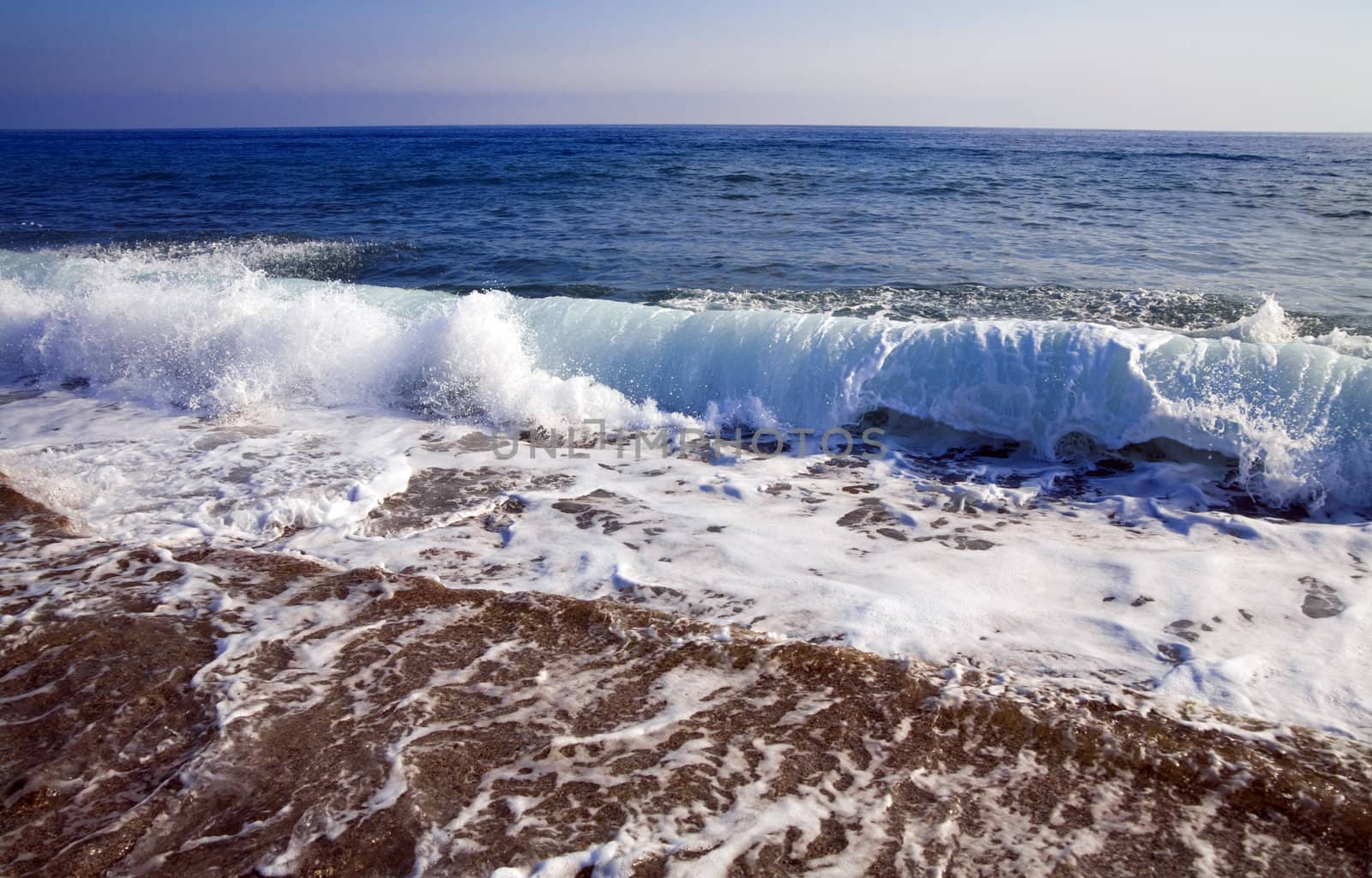 foamy shore blue waves over the horizon in a clear summer day