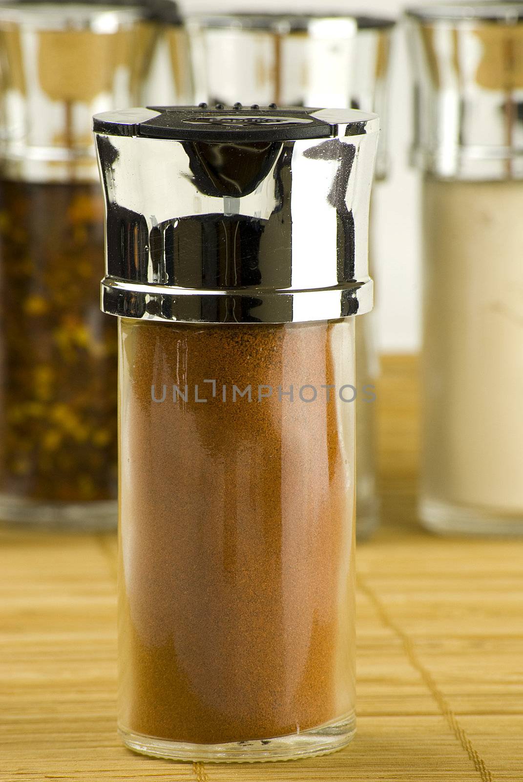 paprika powder in a glass jar on different spices background over wooden mat