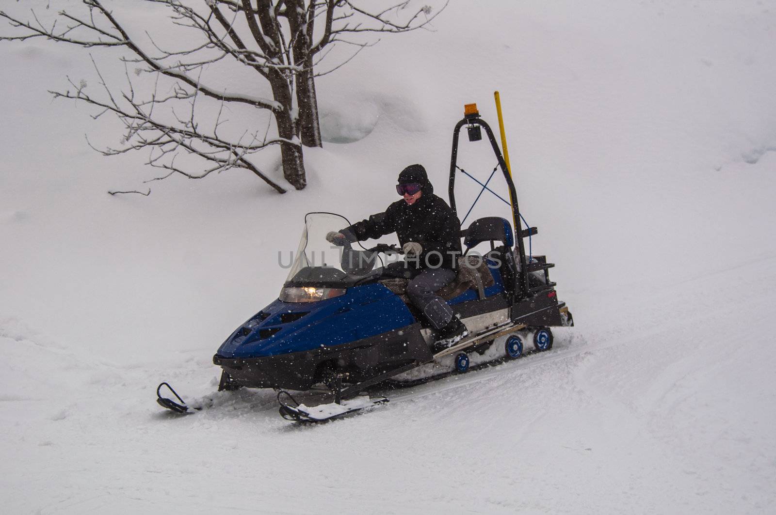 Snow mobile rider driving along skiing piste with his skidoo during snowfall in Montafon, Austria