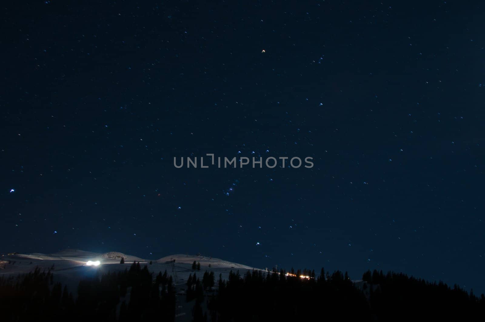 Night panorama of Montafon, Austria with great starry sky and snow groomer preparing the piste