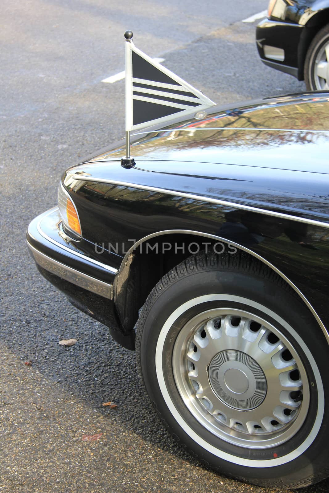 Front detail of a black hearse or funeral car, flags with white lining