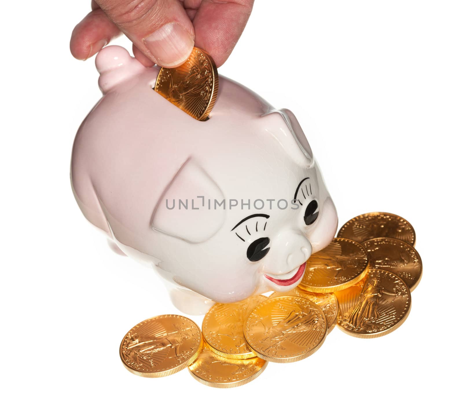 Fingers placing a single gold coin into the slot on a piggy bank and isolated against white