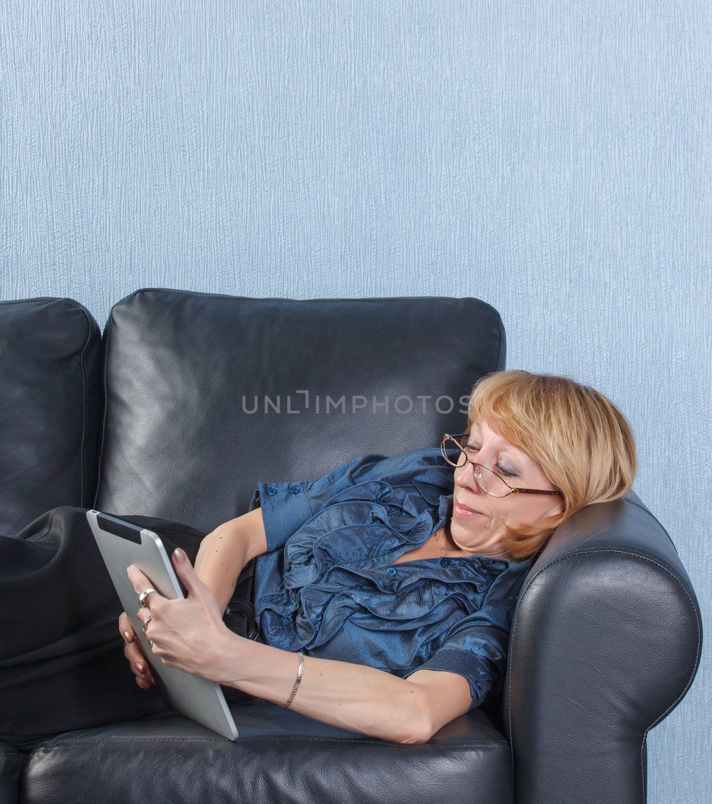 middle aged woman using tablet PC on couch by Discovod