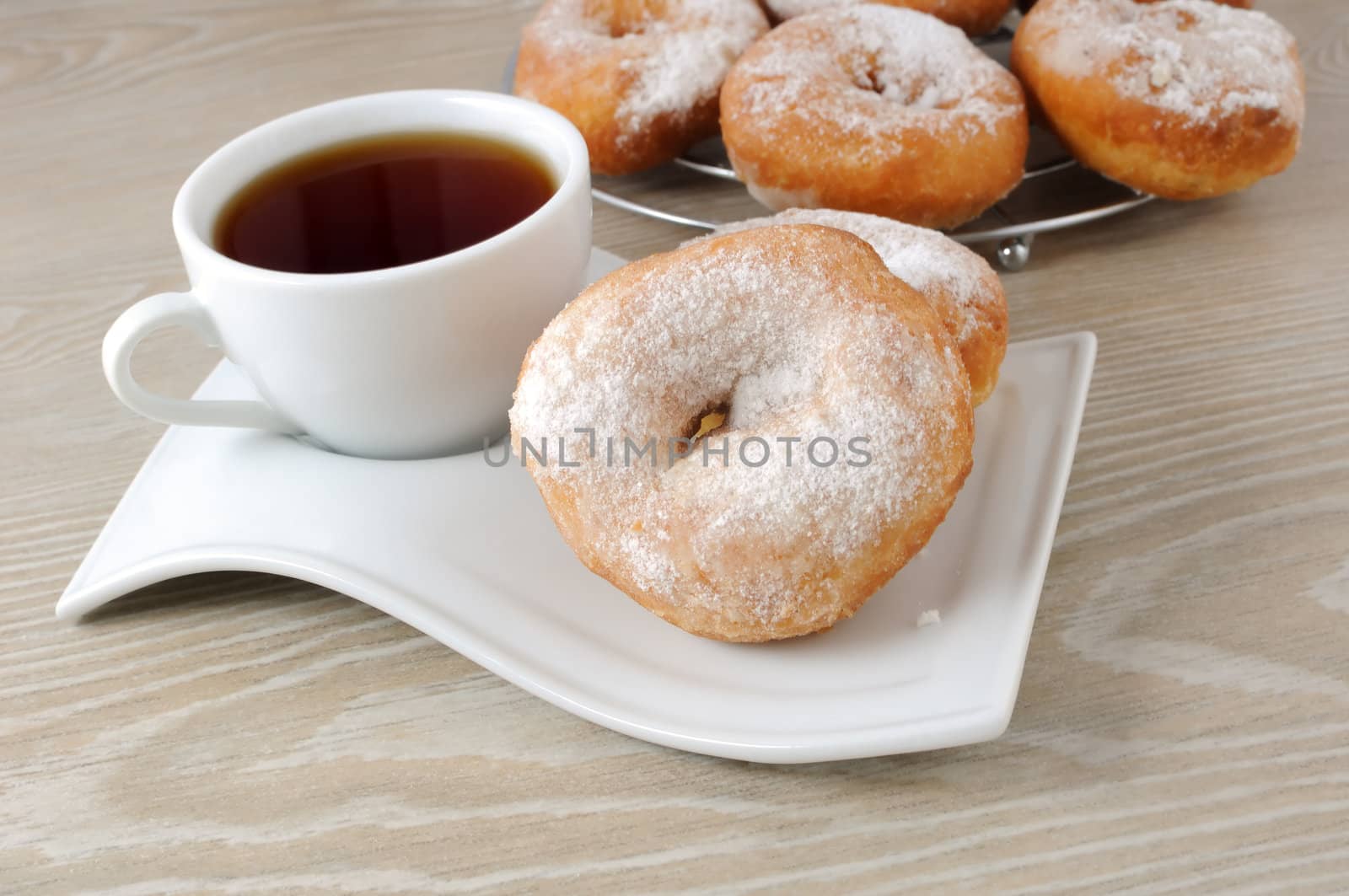 A cup of coffee and donuts in powdered sugar on a plate