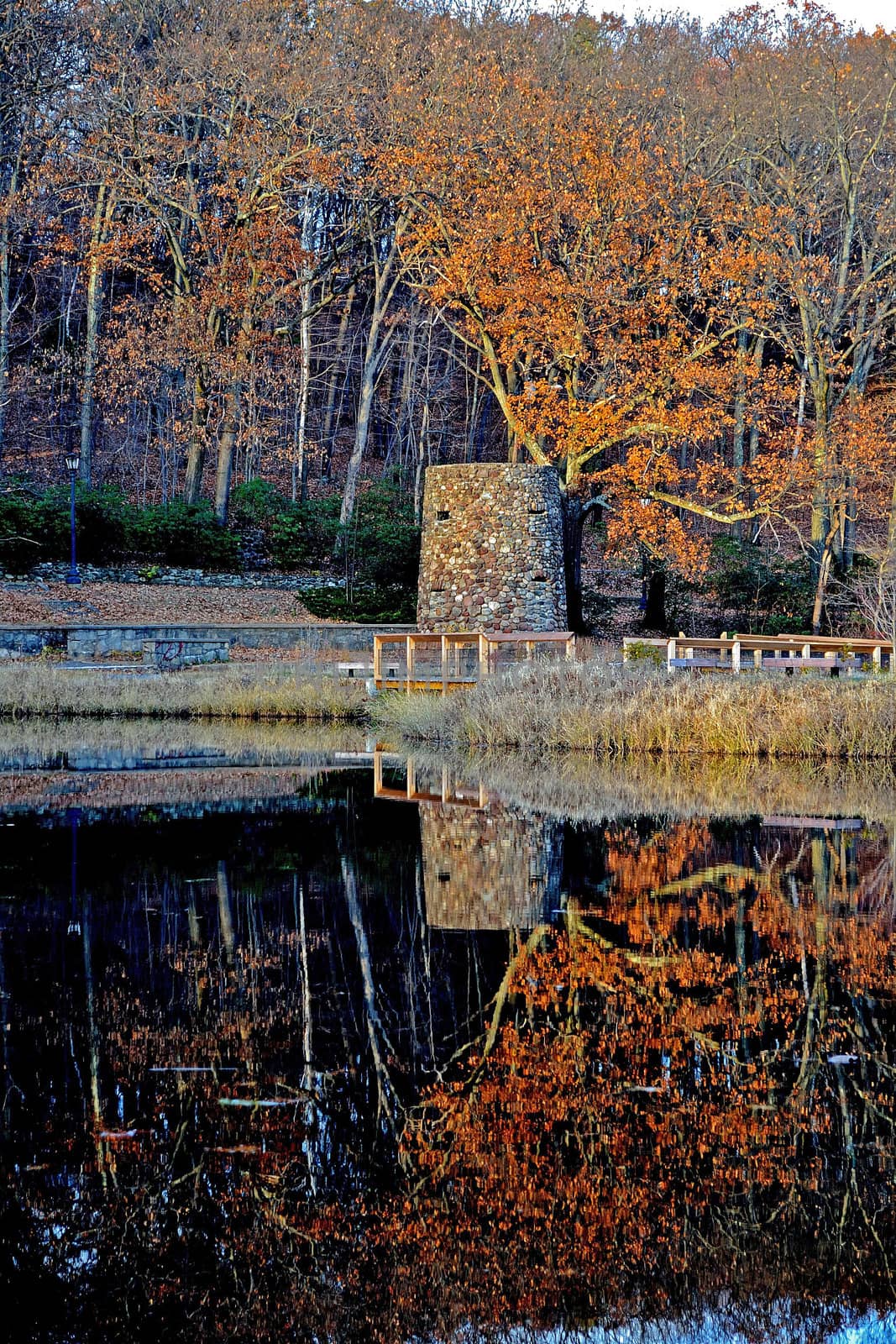 The colorful fall foliage reflected in the mirror like surface of the pond along with the stone tower in Rockwell Park.