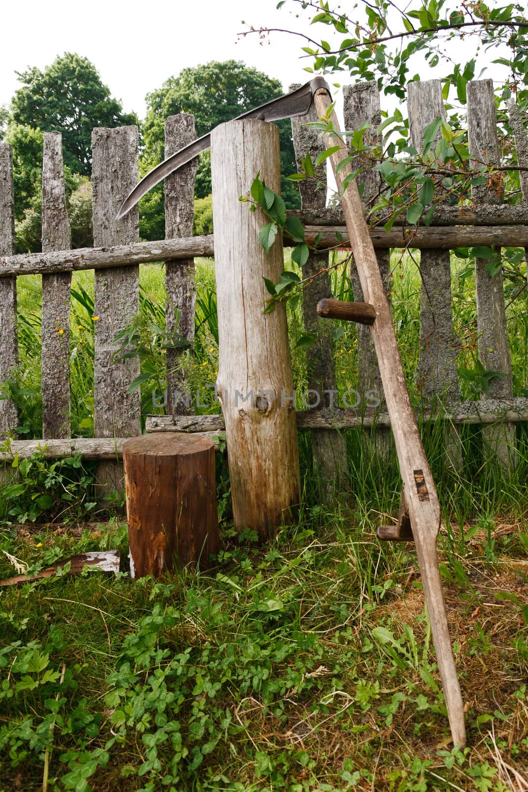 old scythe placed against the wooden fence