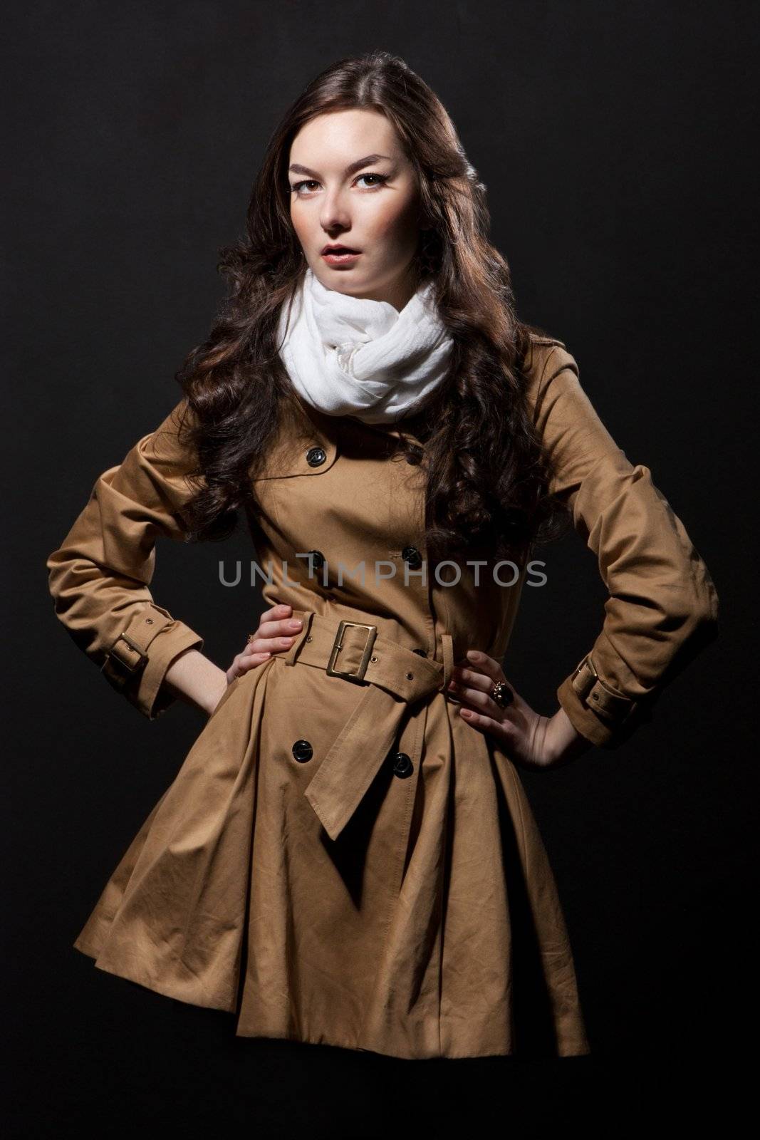 Expressive fashion studio shot of young and beautiful woman wearing brown overcoat on dark background. (Professional makeup and hair style).