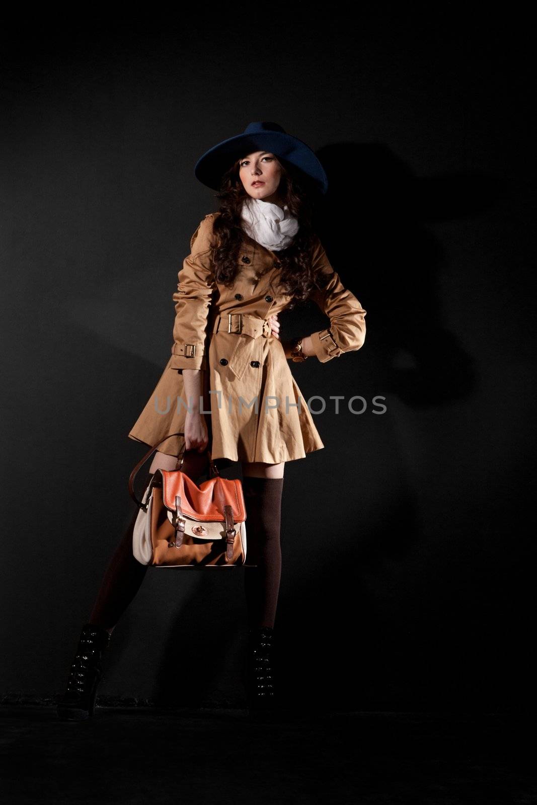 Expressive fashion studio shot of young and beautiful woman wearing brown overcoat on dark background. (Professional makeup and hair style).