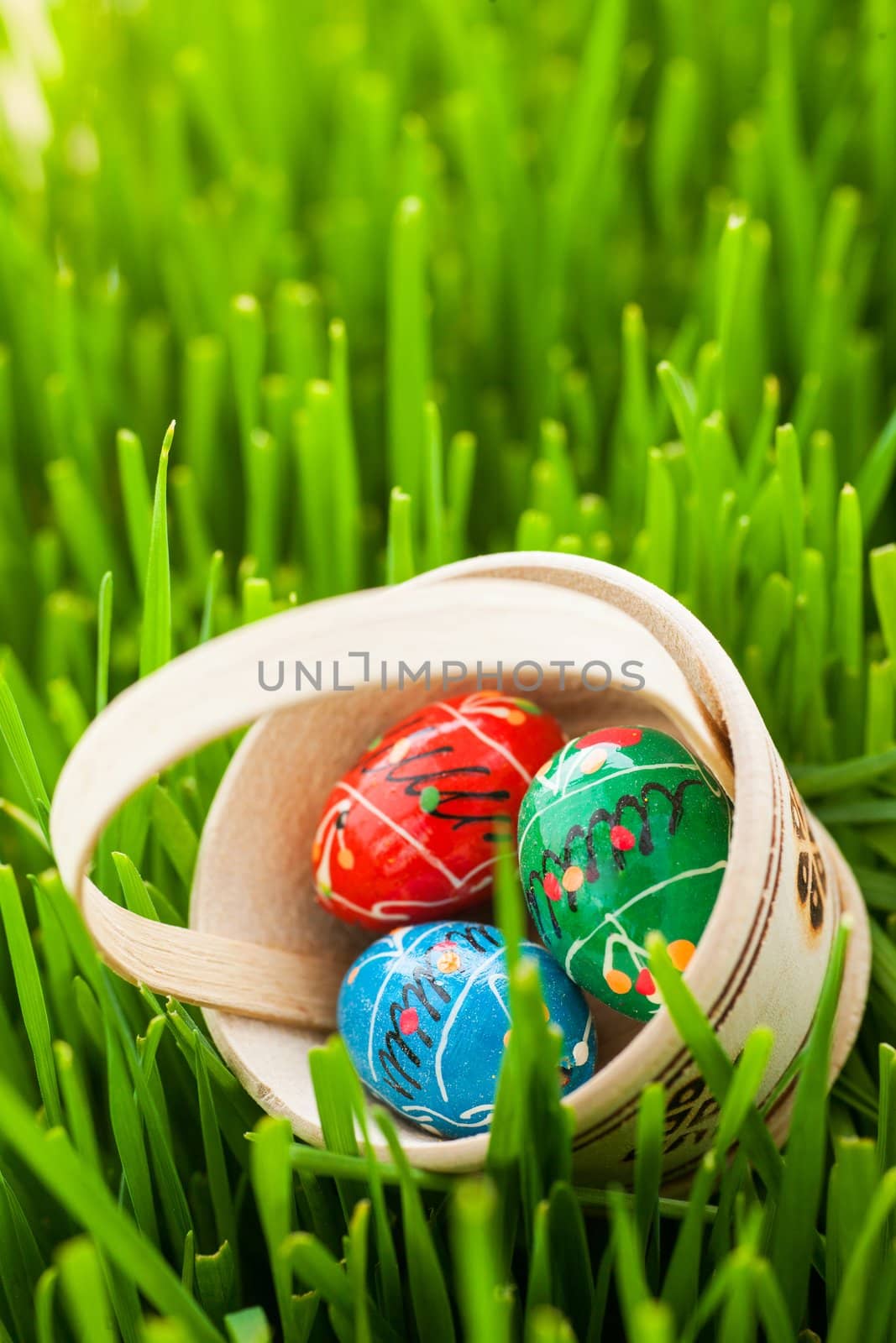 Basket with colored Easter eggs are in green grass. Vertical view