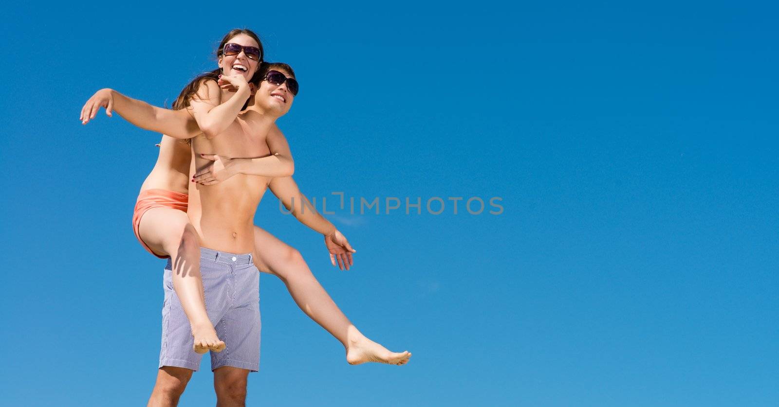 girl sitting on a guy having fun and waving their arms, behind blue sky