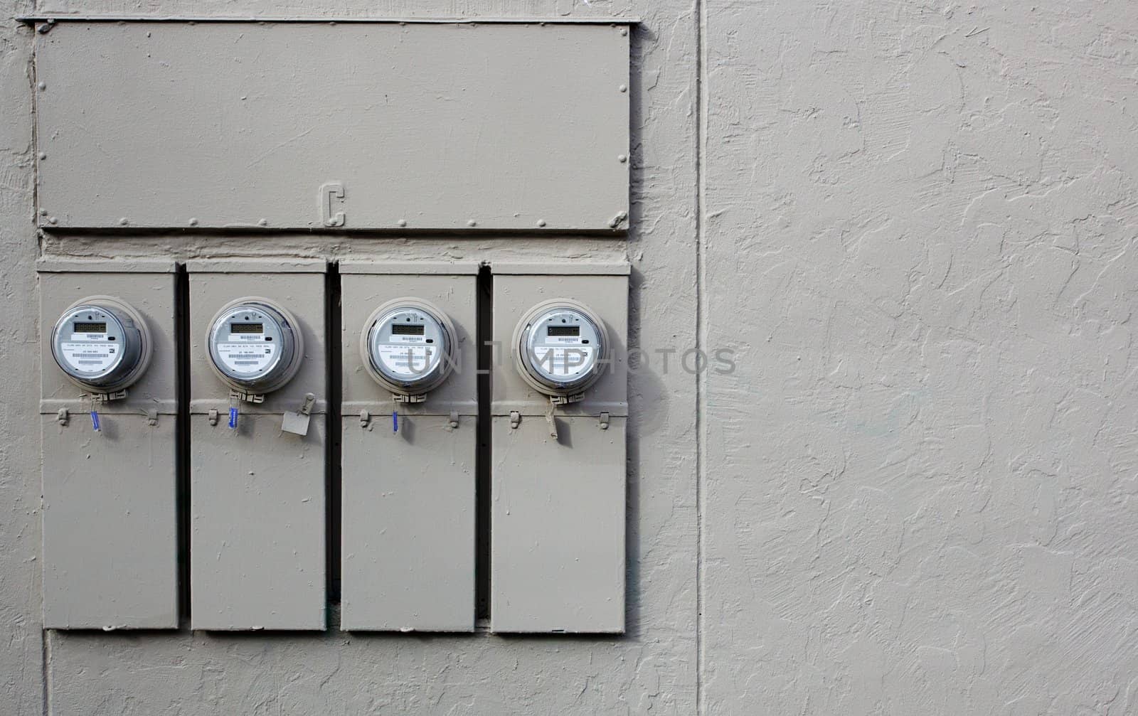 Four Electric Meters on the gray stucco wall of an apartment building