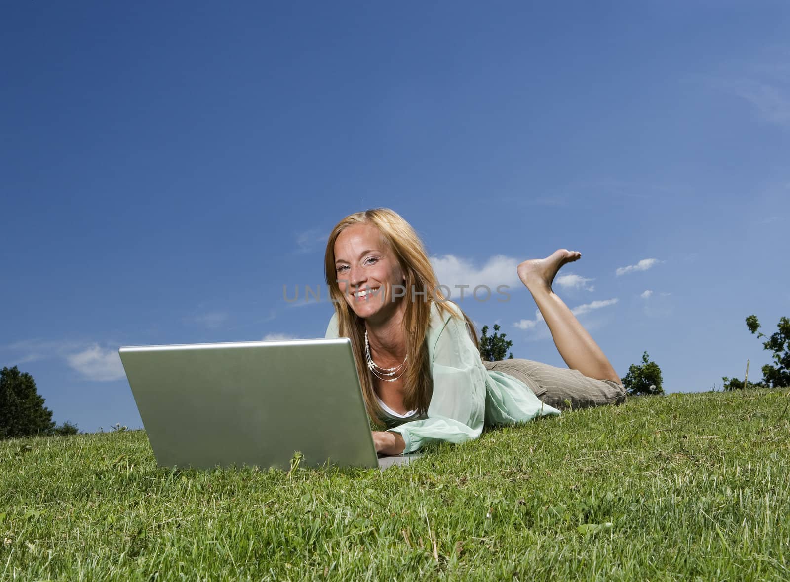 Woman with computer in the grass towards blue sky