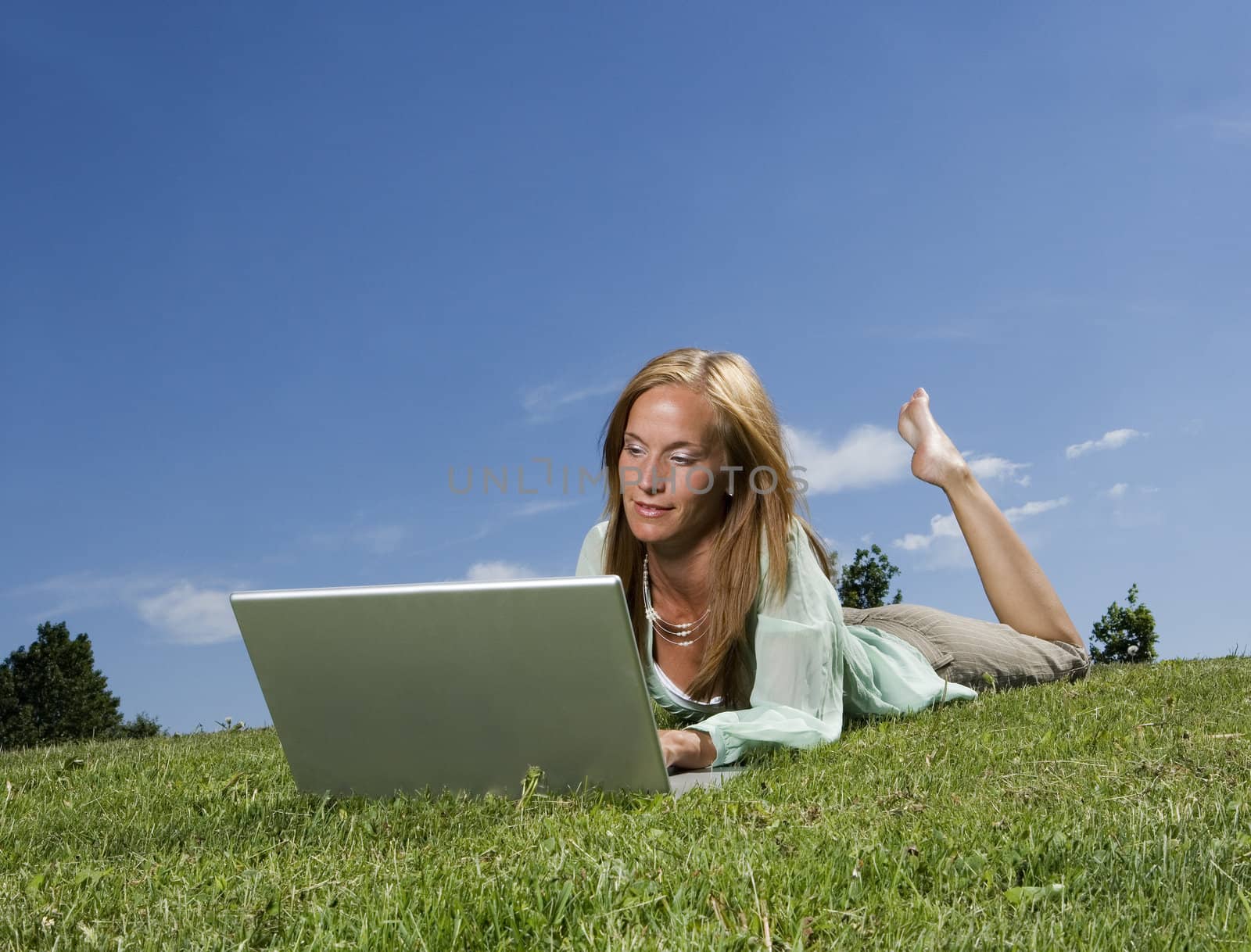 Woman with computer in the grass towards blue sky