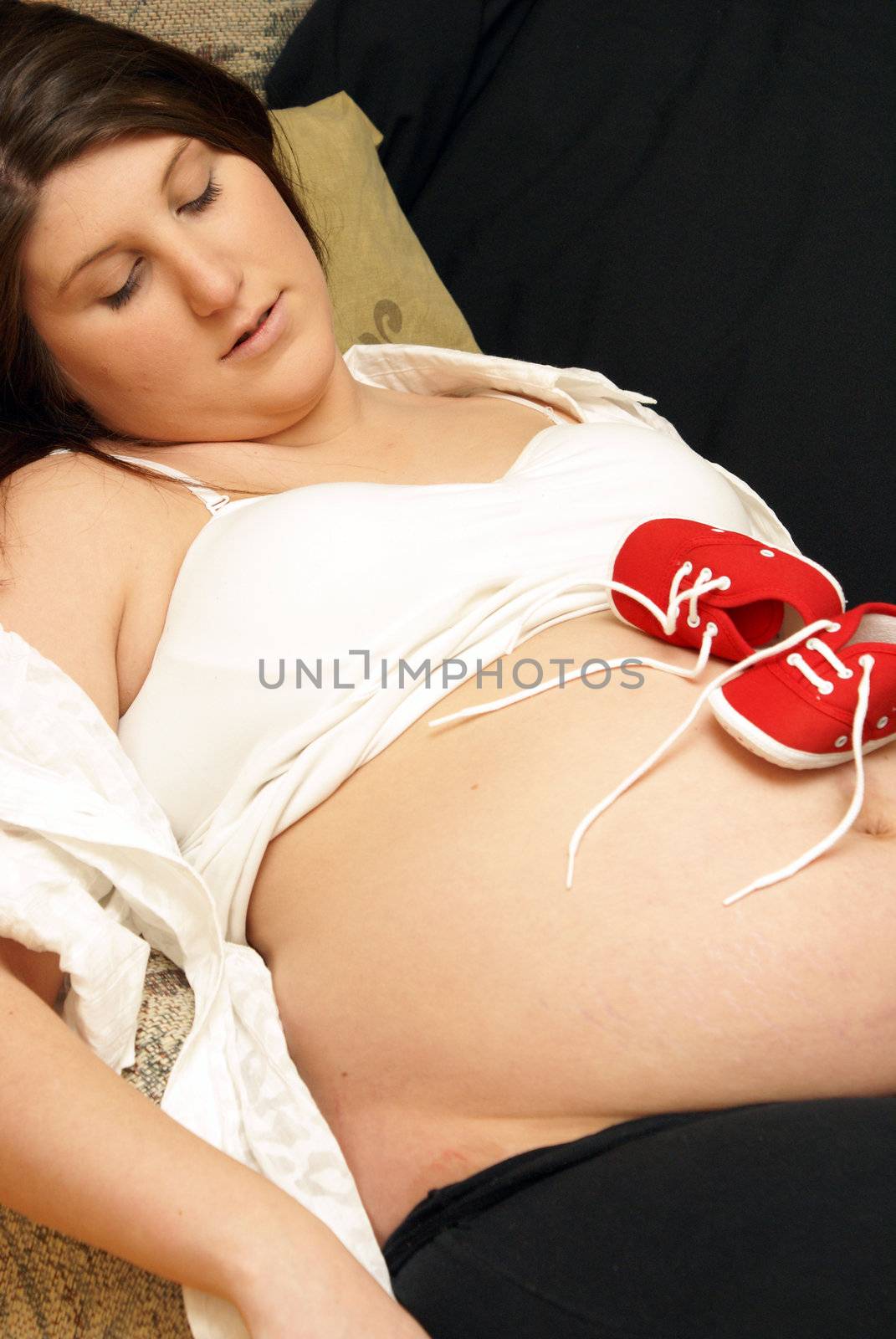 A mother lays back and rests her unborn childs shoes on her belly.