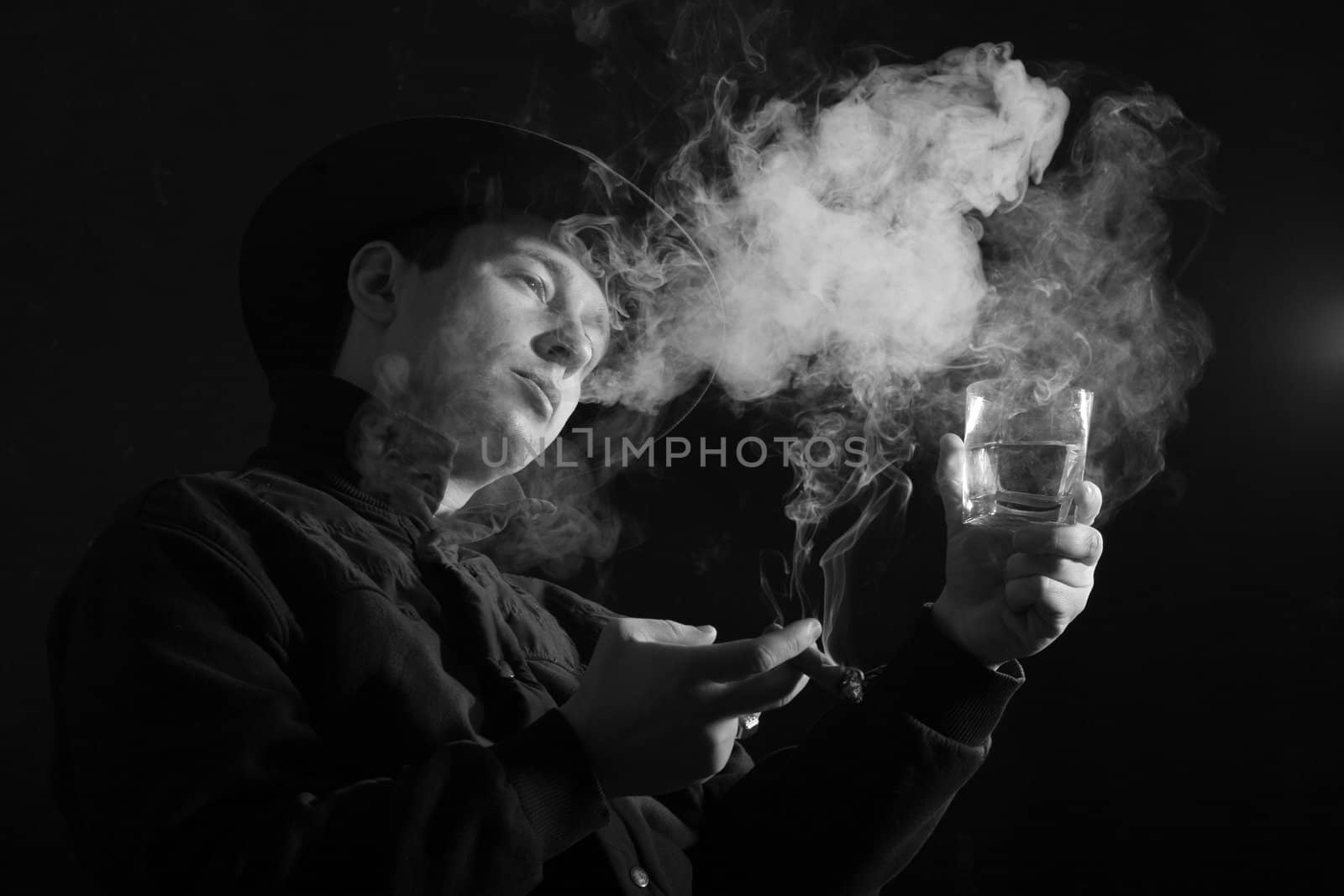 A young man smoking a cigar with a glass of whiskey