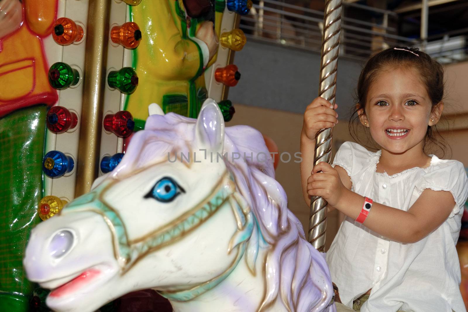 A sweet smiling child is sitting on horse in carousel