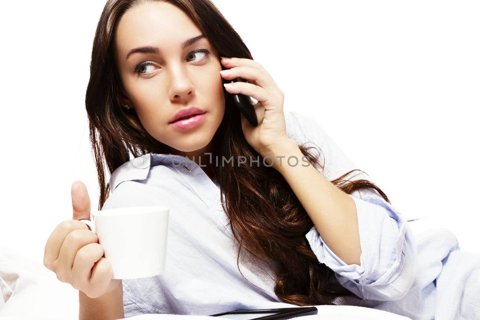 beautiful woman in bed holding coffee while calling with her phone on white background