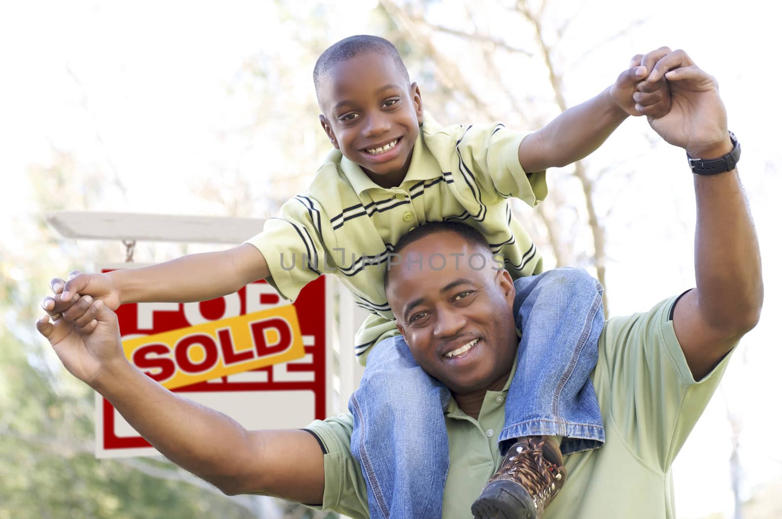 Happy African American Father and Son in Front of Sold Real Estate Sign.