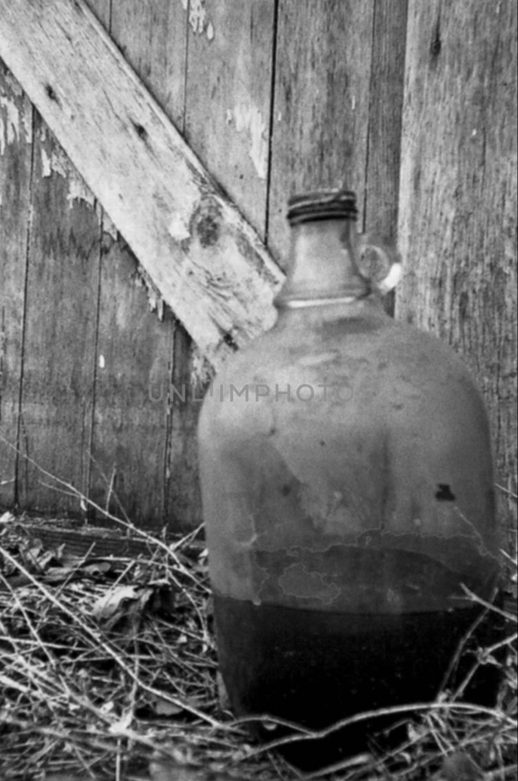 Black and white clear glass whiskey jug next to an old barn.