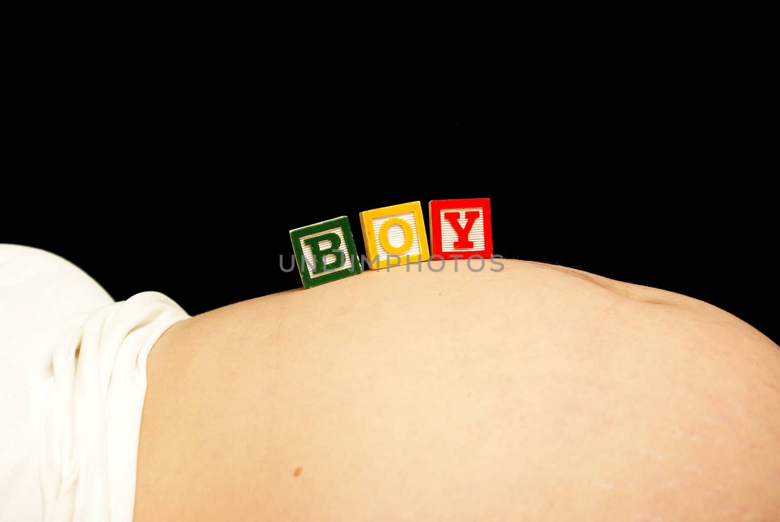 An expecting mother rests some baby blocks on her pregnant belly that spell out the word boy.