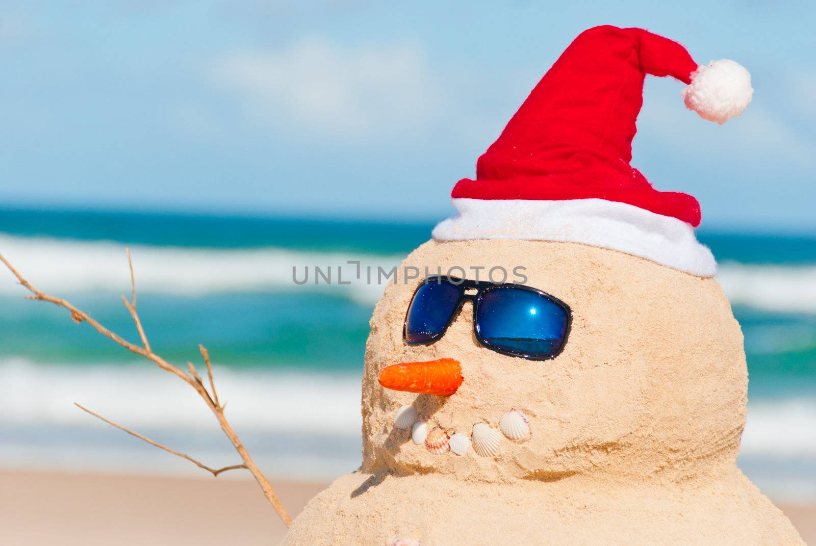 Happy snowman at the beach with sun glasses. His right arm is visible as well