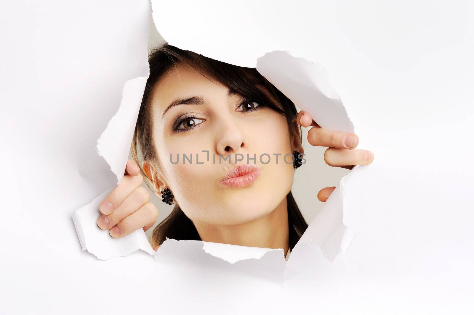 Young girl kissing through hole in white paper