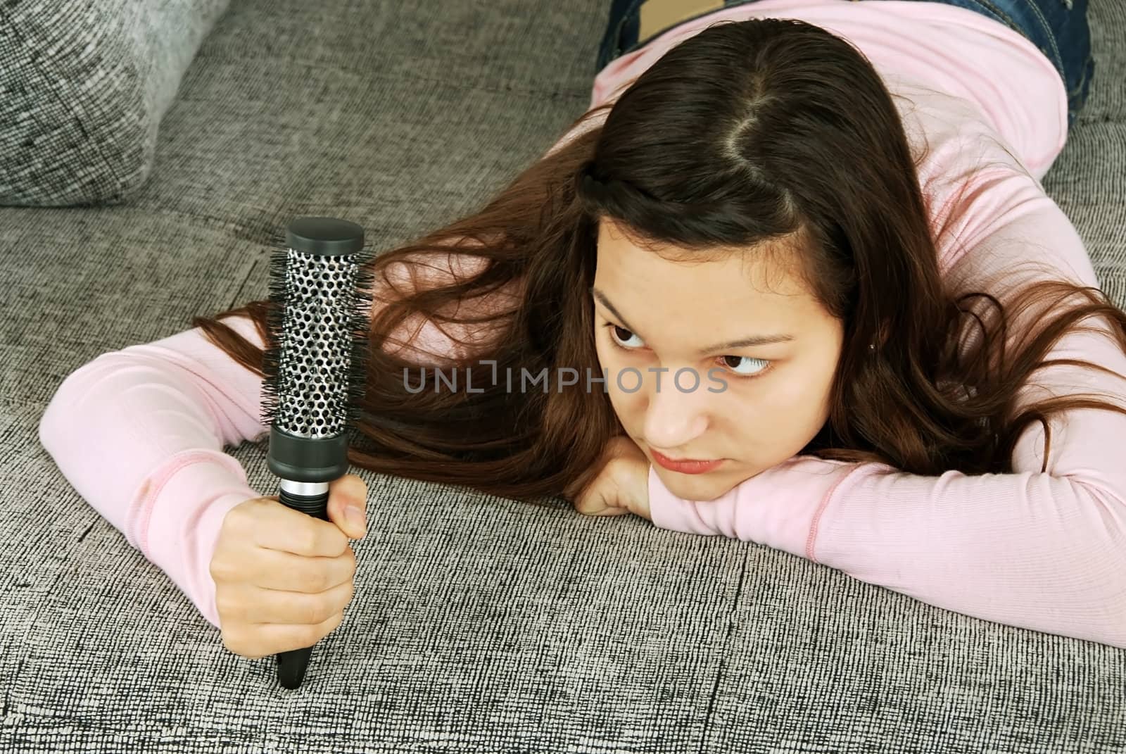 caucasian teenage girl lying on stomach looking at her hairbrush, thinking about her hairs