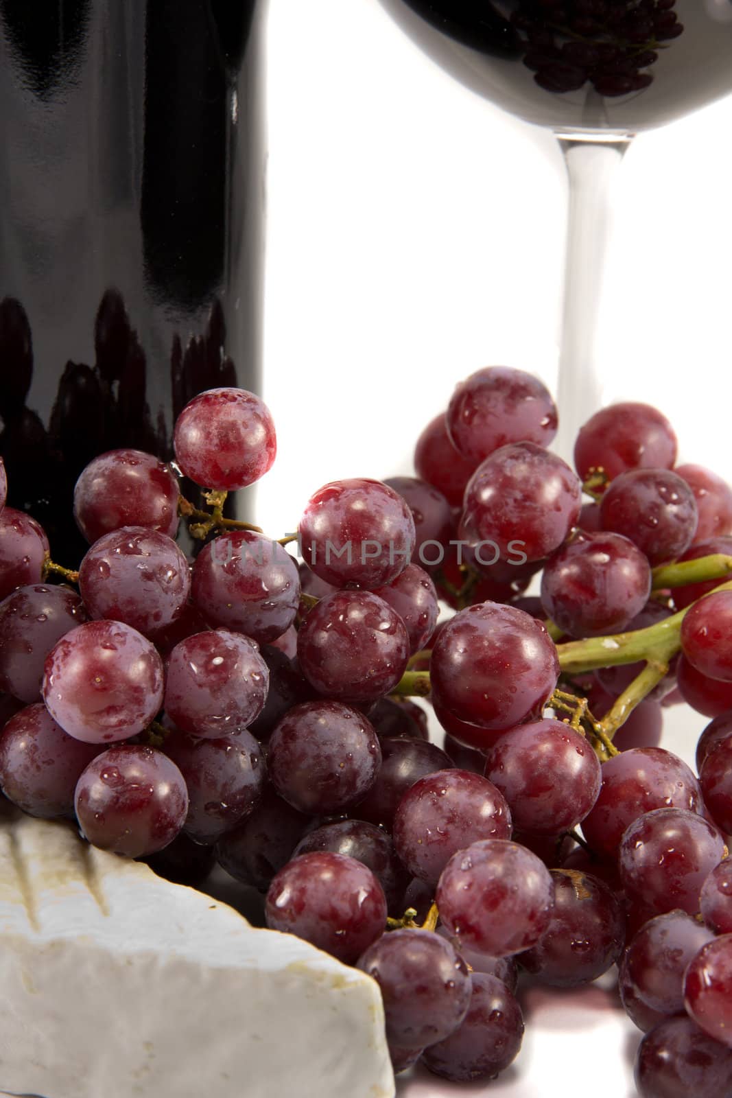 Picture of some grapes and a piece of brie with red wine in the background