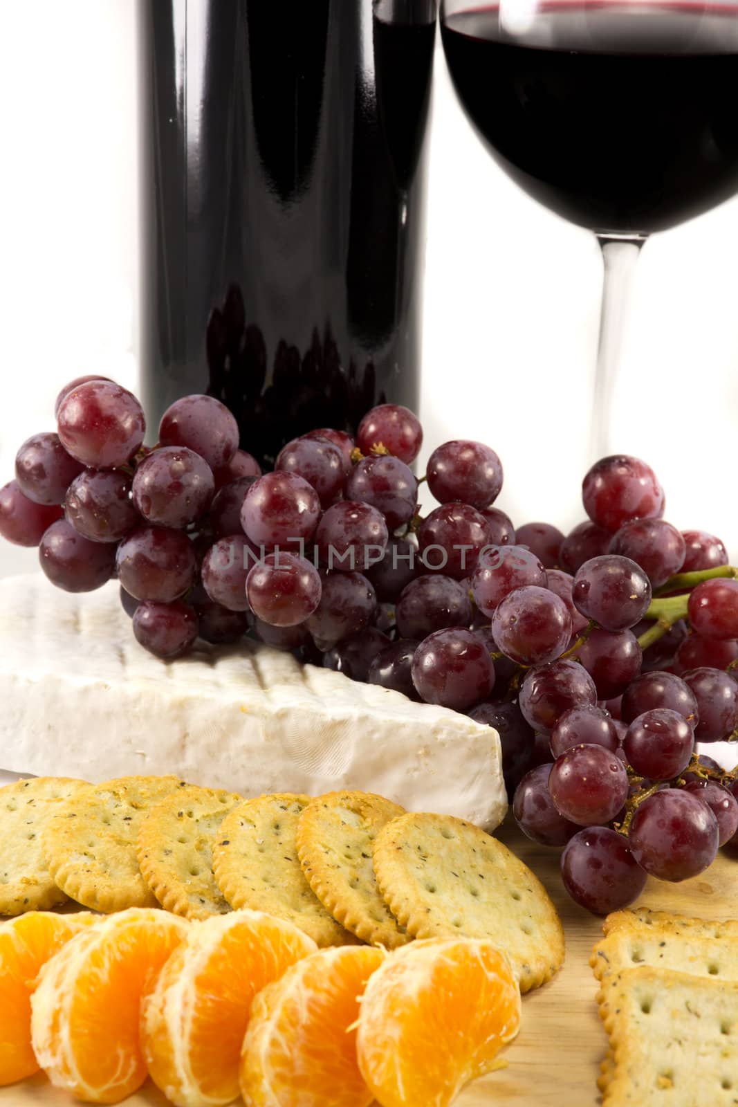 Picture of some grapes brie and some clementins with a bottle of red wine in the background