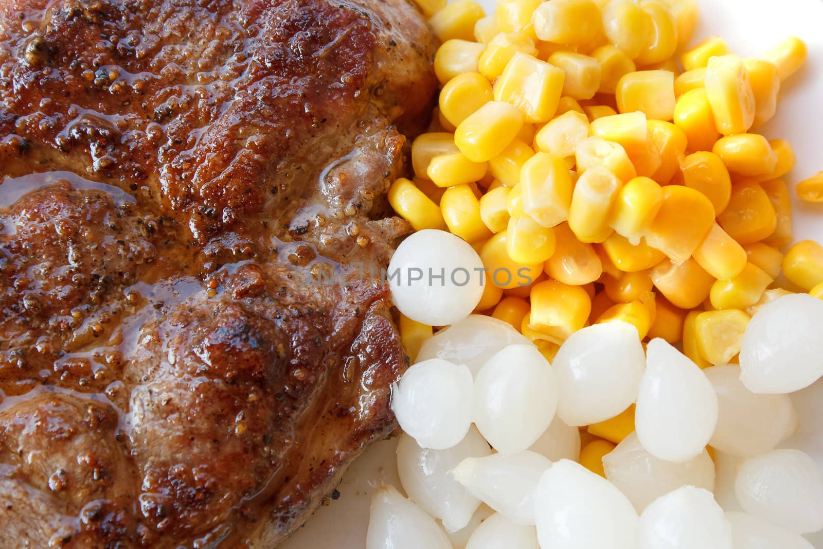 grilled pork steak with corn and small onions on plate