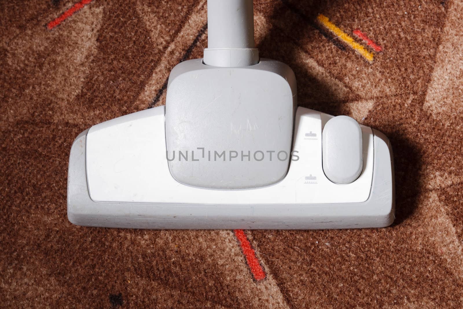 Close-up of a vacuum cleaner picking up dust and dirt from a brown carpet