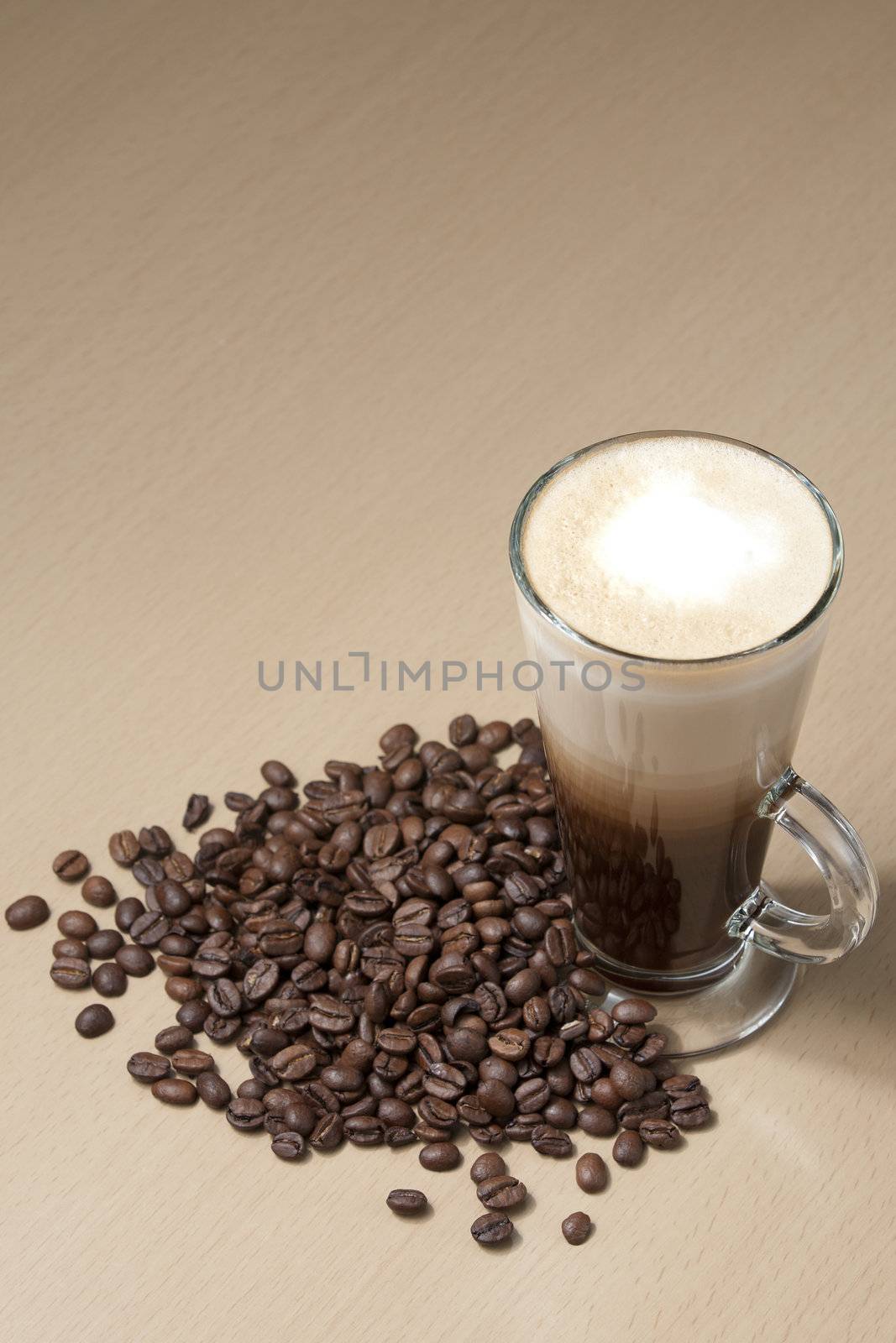 Coffee with froth and coffee beans below on the table. Vertical