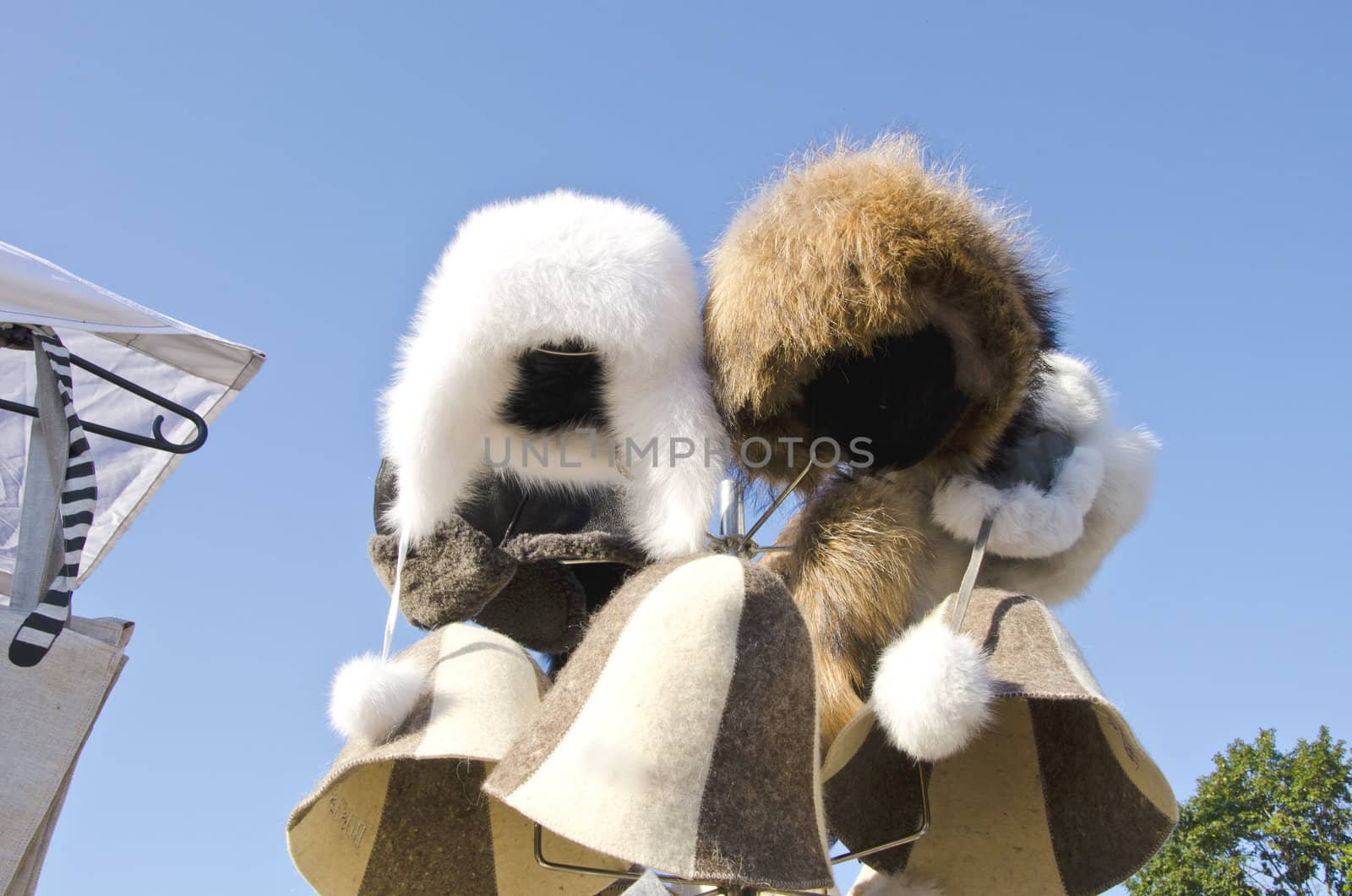 Winter fur hats cap sold at market outdoor street fair on background of blue sky.