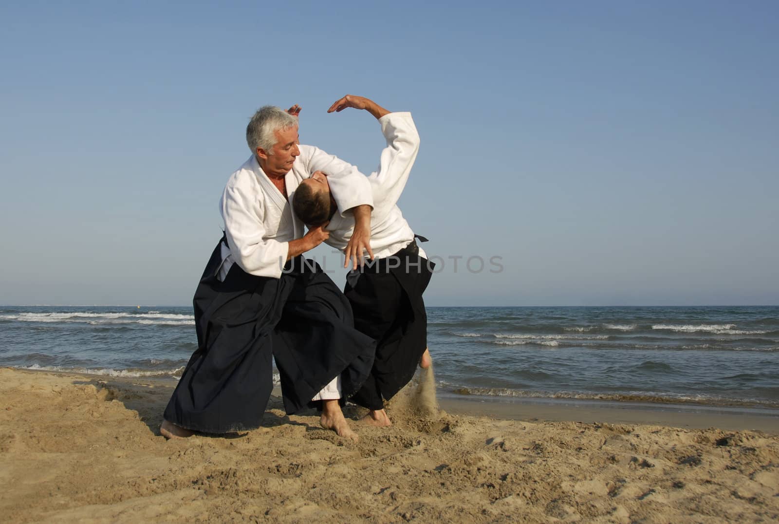 Two adults are training in Aikido on the beach