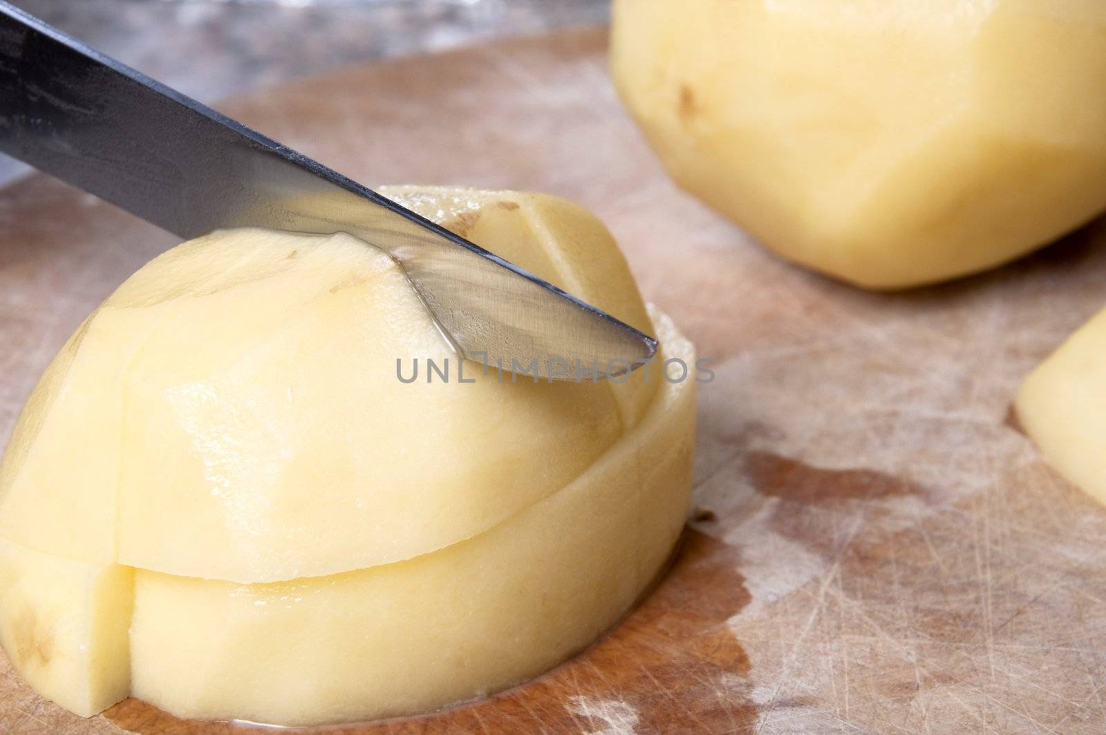 Close up action shot of potatoes being chopped on an old wooden chopping board, with visible cut marks.  Counter top visible in background.  