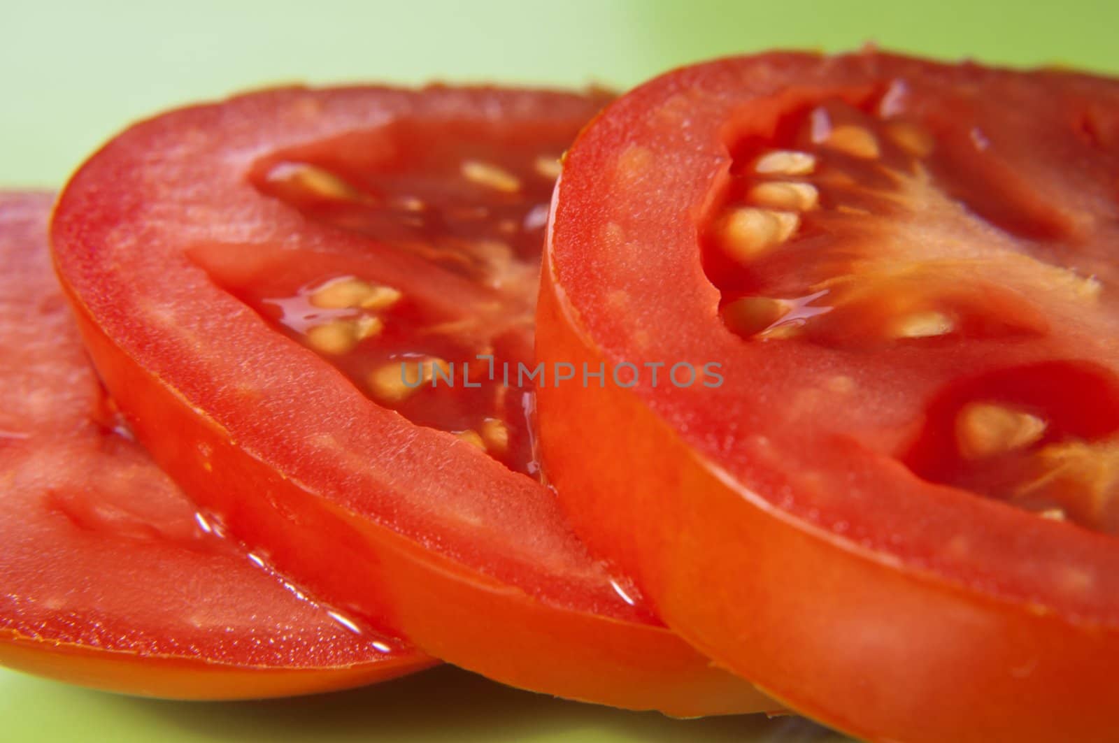 Macro shot of three tomato slices on a green surface.  Skin and seeds visible.