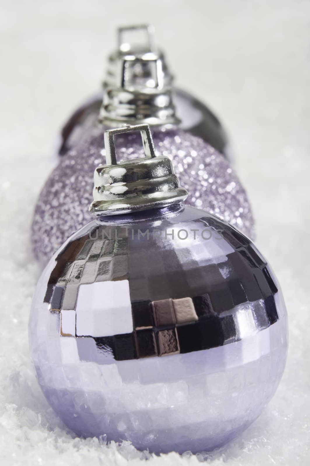 Close up (macro).  A row of three mauve Christmas baubles with shiny and sparkling textures, resting on a fake snow surface.  