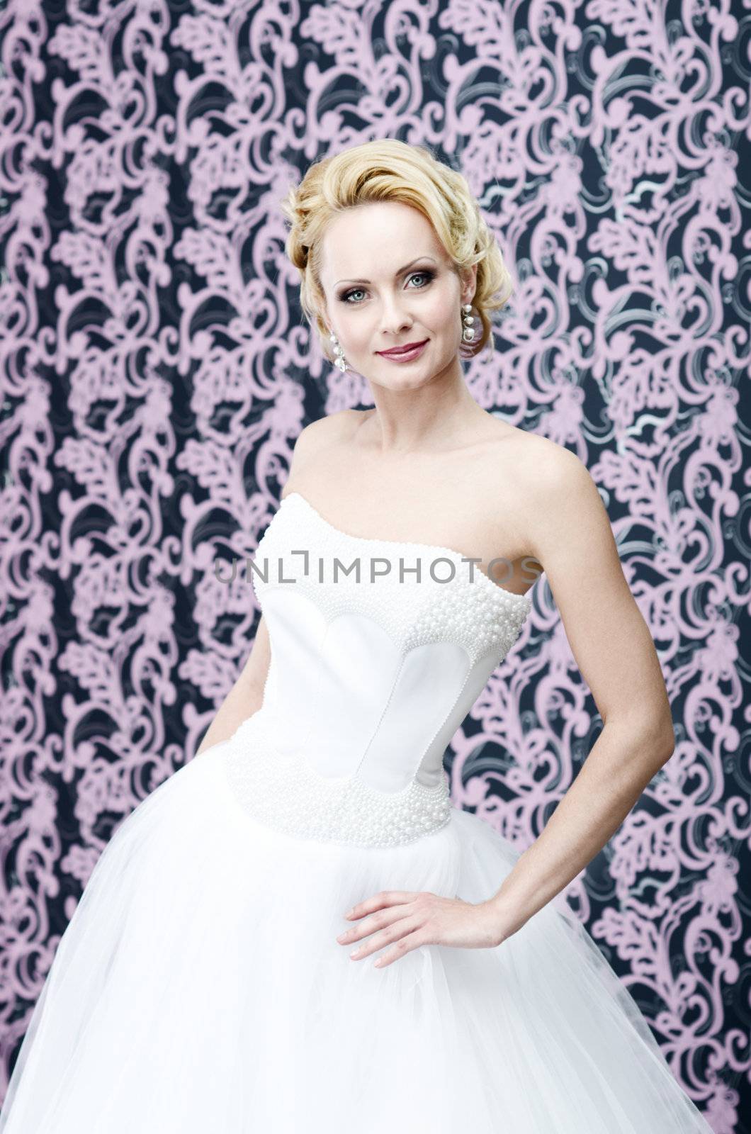 20s yeared blonde bride posing in white wedding dress. She is slightly smiling