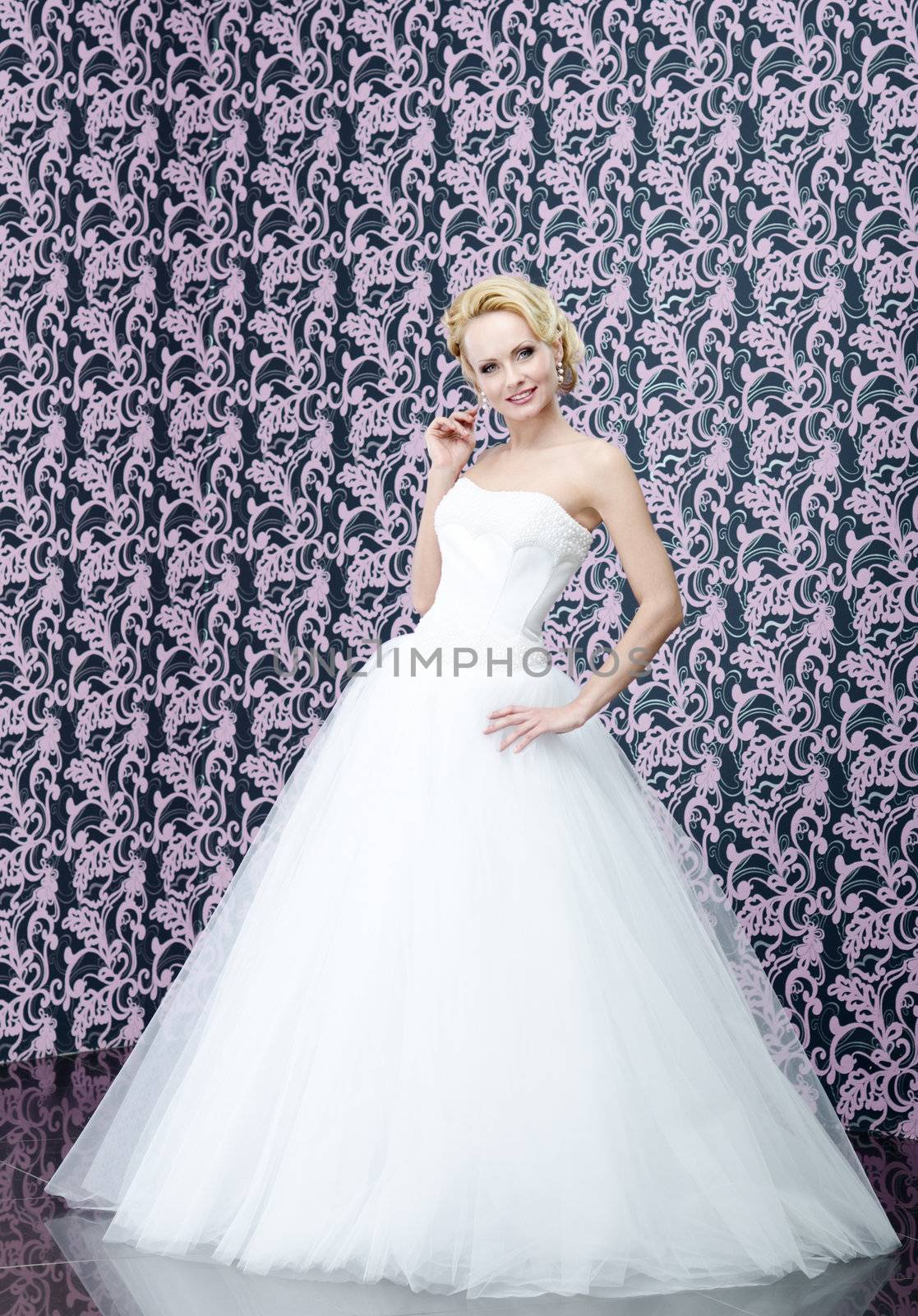 Young adult blonde bride full length portrait. She is touching her curly hair and smiling