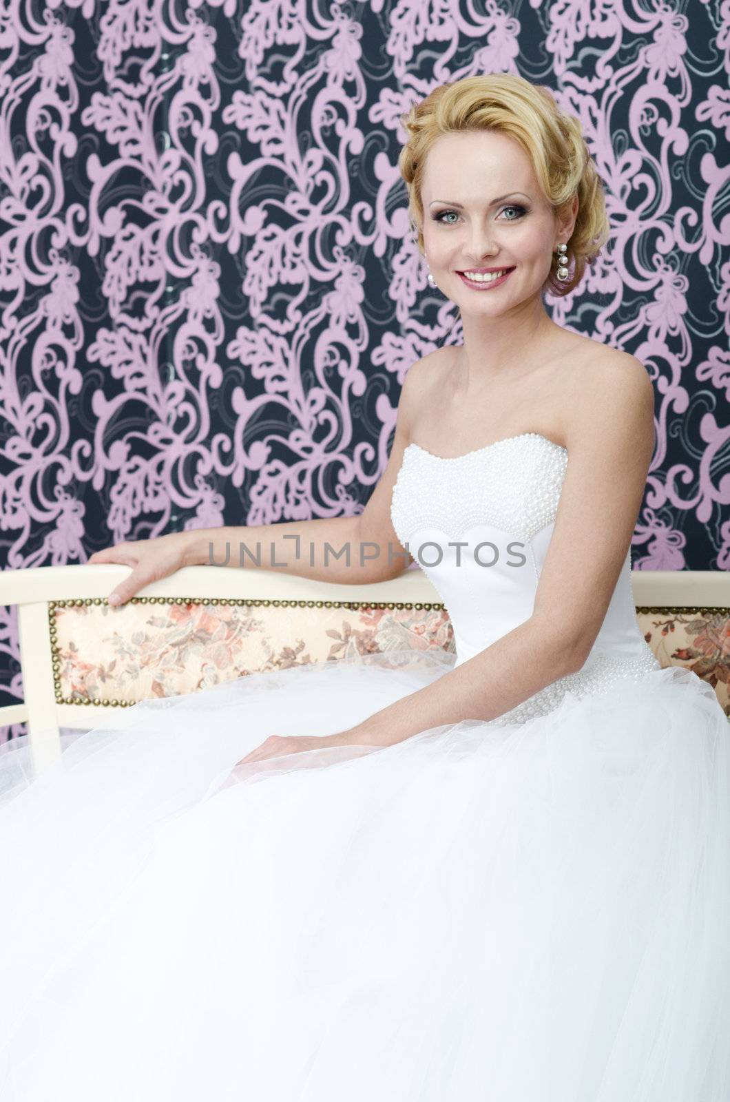 Studio shot of the young adult caucasian bride. She is sitting on the bench with smile on her face