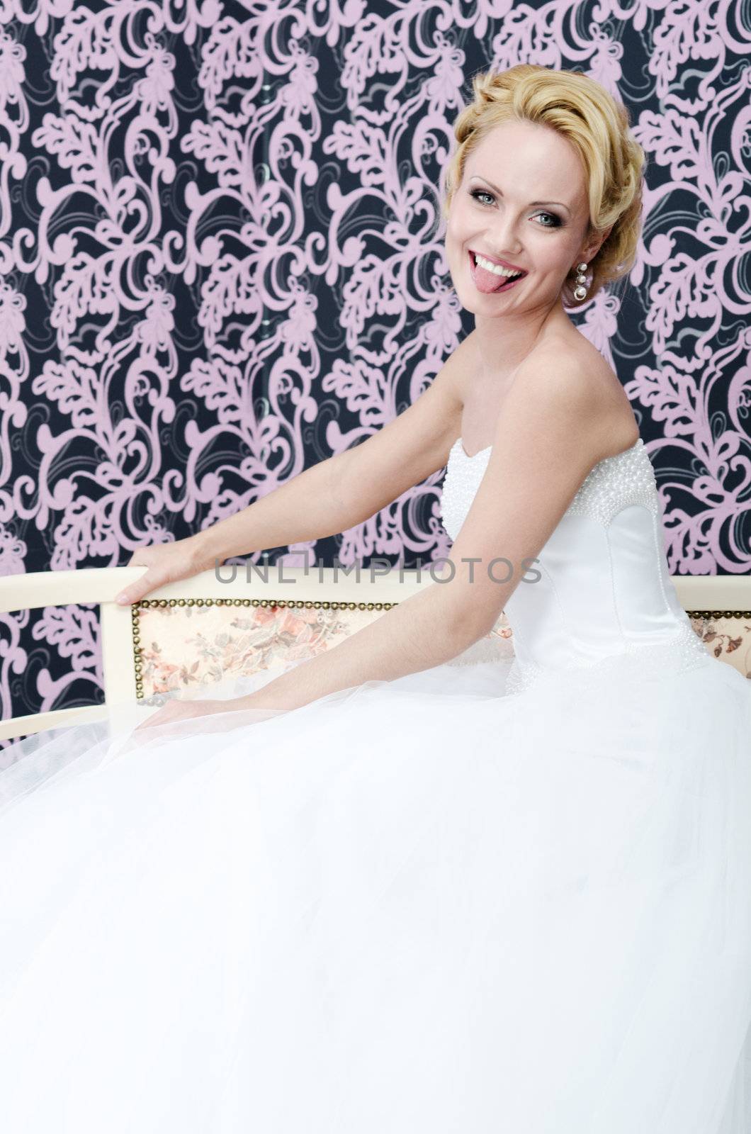 20s aged young adult bride is sitting on a bench. She is smiling and put out her tongue.