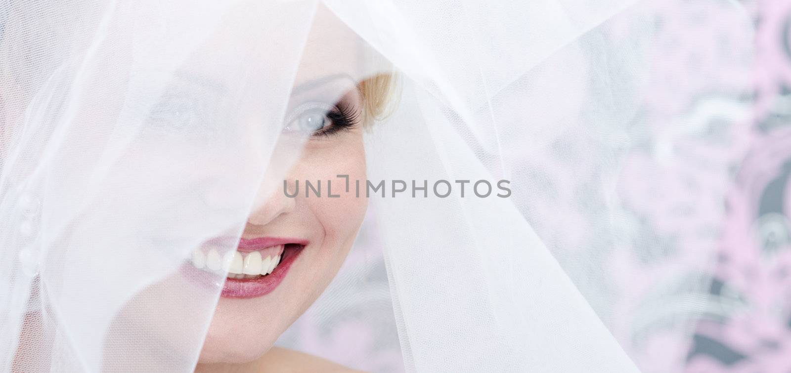 Close up image of the smiling adult bride. Transparent veil cover her face
