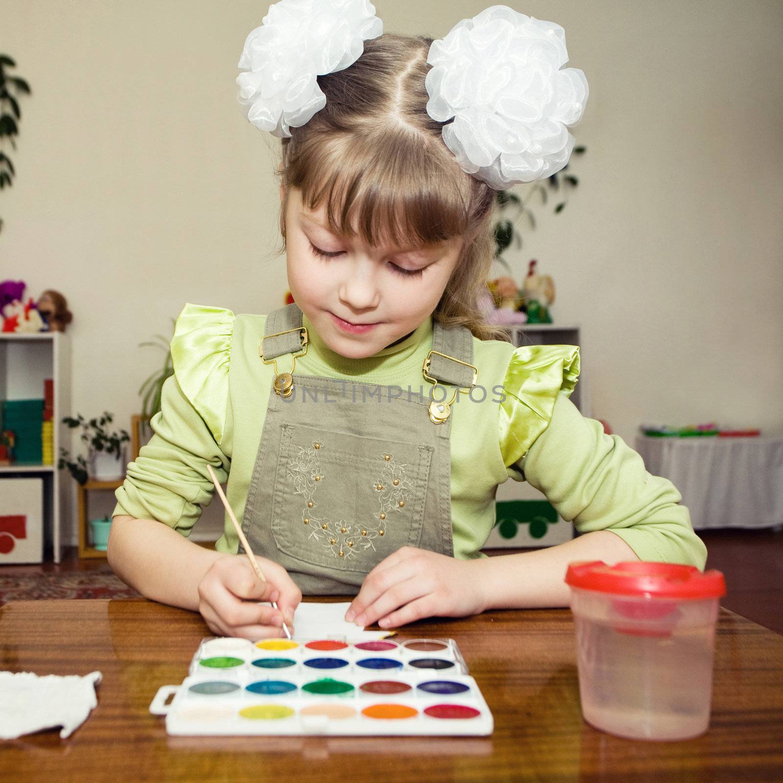 A little girl sitting at the table and painting gouache in a kindergarten