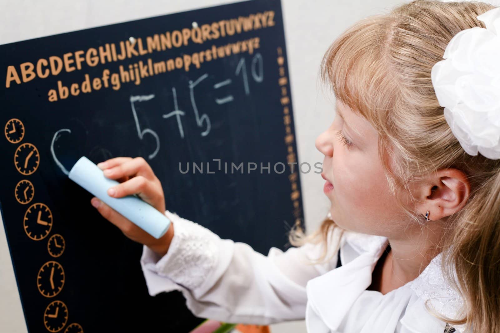 Little girl standing near blackboard. Writing on it.