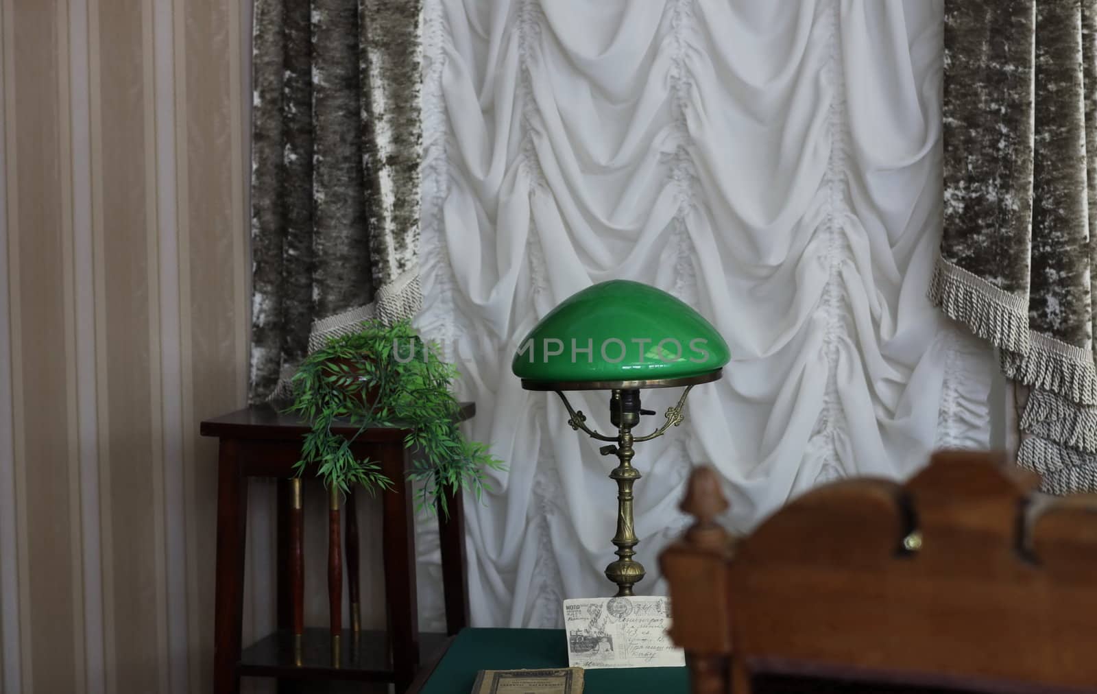 fragment of the interior cabinet,  table at the curtained windows  and bronze lamp with green shade