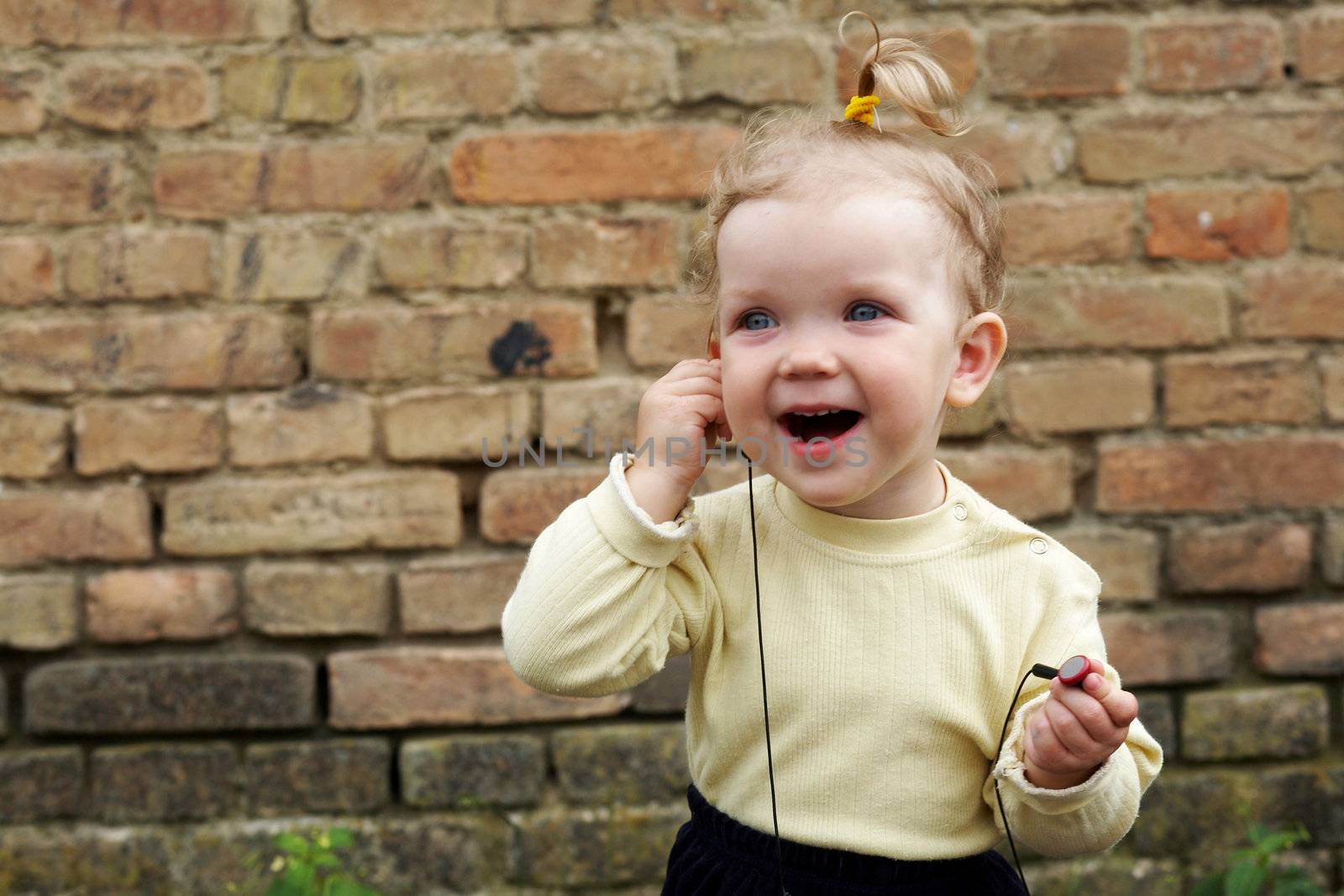 The baby-girl listens to music on a background of a brick wall