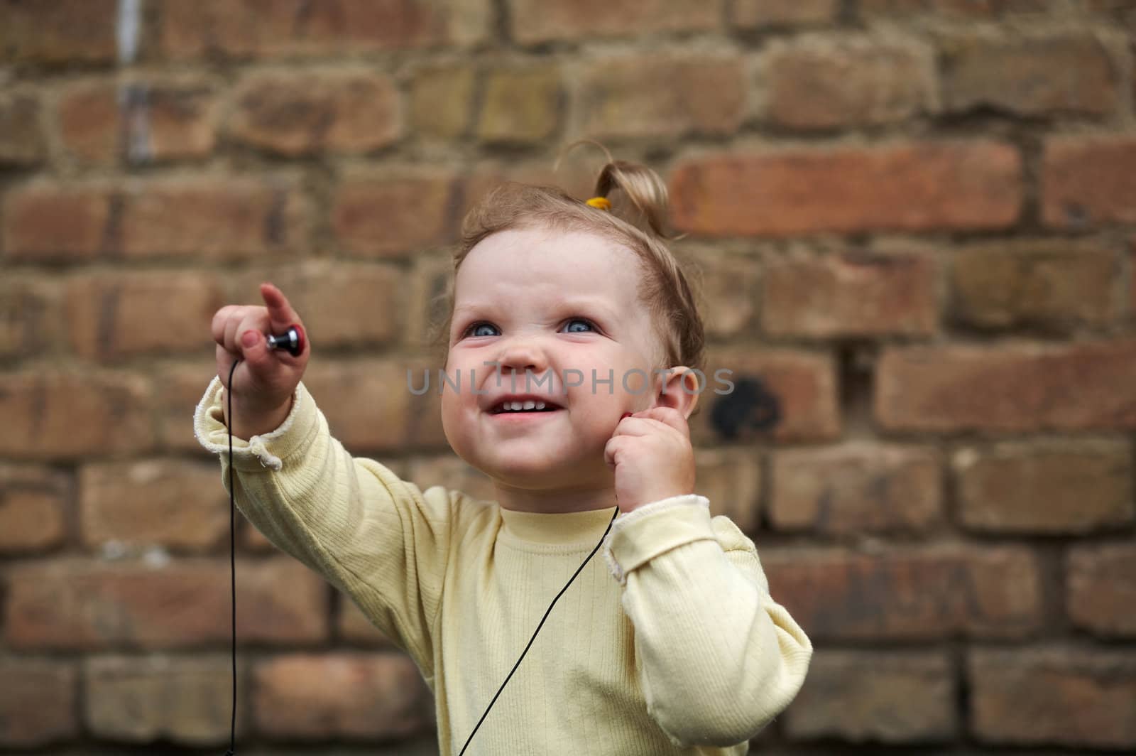 The baby listens to music on a background of a brick wall