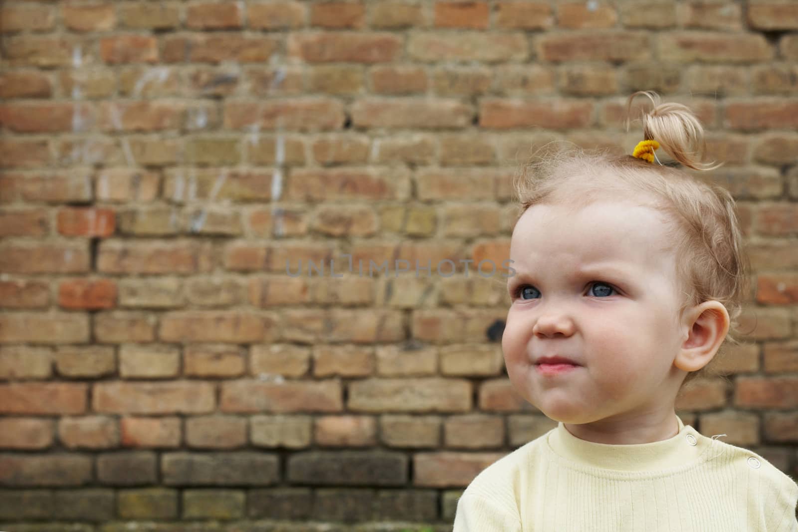 An image of baby-girl near a brick wall